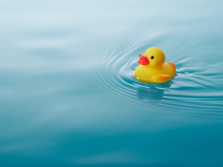 yellow rubber duck swimming on water causing waves and ripples
